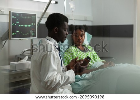 African american practitioner doctor discussing medication treatment to sick patient explaining flu symptoms during medical appointment in hospital ward. Young woman resting in bed taking painkiller