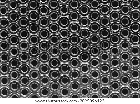 Smooth vertical rows of hexagonal chrome-plated nuts, standing on the side faces, on a black background, close-up.