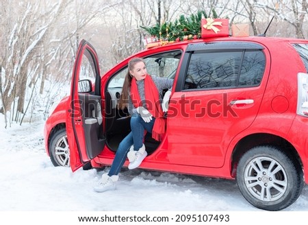 Beautiful young woman sits in red car decorated for Christmas in winter forest during Xmas and winter holidays
