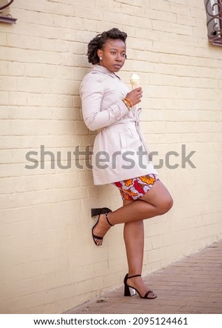 Young African American woman eating pink ice cream in a crispy waffle cone, lifestyle, city walk, theism.
