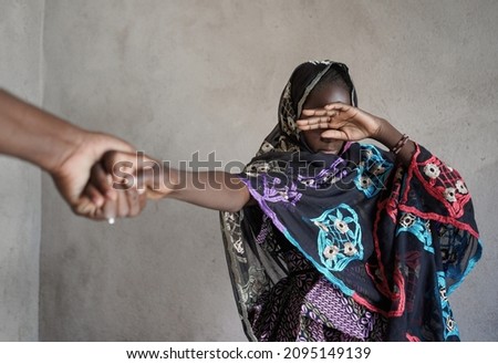 Veiled black African girl with her hand covering her eyes, pulled by the hand of an adult towards an atrocious fate; girl child abuse concept Royalty-Free Stock Photo #2095149139