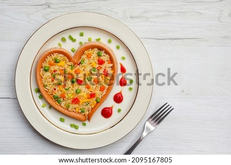 Fried rice with carrots,onions,tomatoes,green peas,spring onions,eggs and soy sauce in heart shaped sausage on plate with wooden background.Healthy food idea for Valentine's day.Top view.Copy space

 Royalty-Free Stock Photo #2095167805