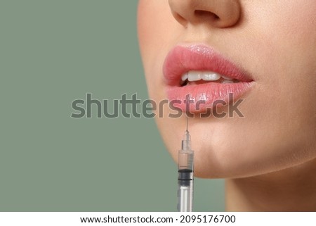 Young woman receiving filler injection in lips against color background, closeup