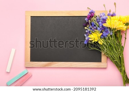 Blank chalkboard, bouquet of flowers and pieces of chalk on color background