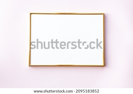 Empty frame on gentle pink background. A golden photo fra,e lying on background with place for your text. Mock up.