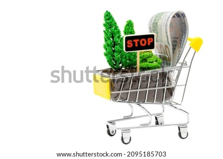 Miniature shopping trolley with toy forest set-up, dollar bills and a stop sign isolated on white. The concept of spreading the word about the impacts of illegal logging.