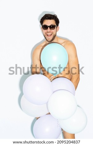 Handsome Caucasian Man In Sunglasses While on Party Or Club Presentation Wearing Contrasty Underware Outfit and Holding Bunch of Colorful Airballoons. Vertical Image