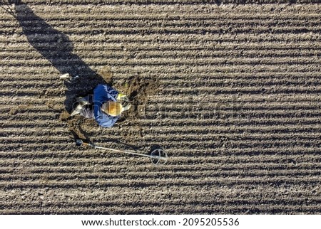 Metal detectorist searcing for ancient metal objects on a big field, seen from a birds perspective