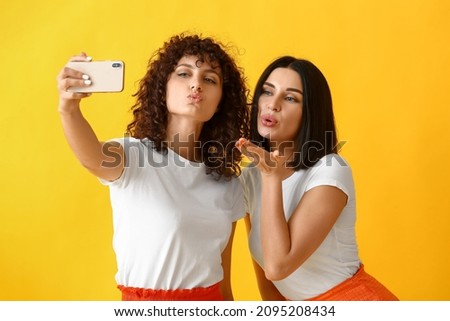 Young sisters giving air kiss and taking selfie on color background