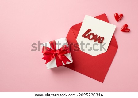 Top view photo of saint valentine's day decorations small hearts white giftbox with red bow open red envelope with paper card and inscription love on isolated pastel pink background with copyspace