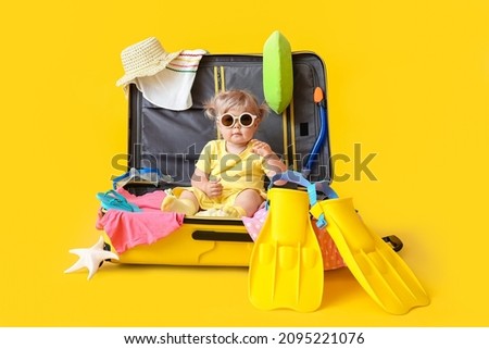 Cute baby girl in suitcase with belongings on color background