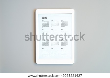 tablet computer with an open app of calendar for 2022 year on a gray background. concept business or to do list goals with technology using. top view, flat lay
