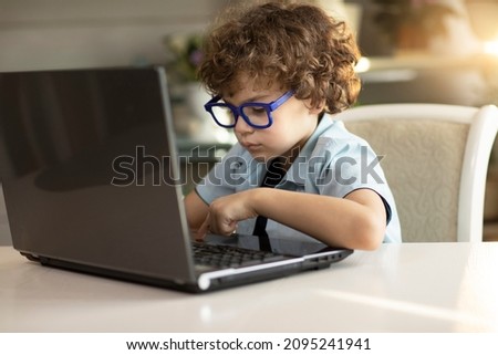 Curly boy in glasses is engaged in a laptop book, carefully looks at the monitor. High quality photo