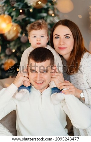 portrait of happy family by the Christmas tree. mom, dad and little son in a room decorated for the New Year's holiday. family traditions. parenthood