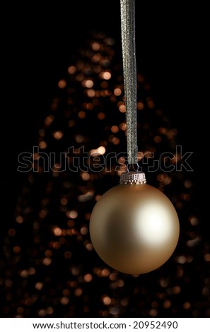 Gold colored ornament with lit Christmas tree in background