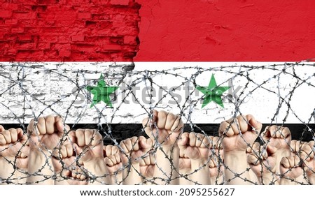 Barbed wire against the background of the inflicted flag of Syria and raised fists
