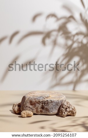 Abstract minimal nature scene - empty stage and composition of stones on beige background and soft shadows of grass and leaves. Pedestal for cosmetic product and packaging mockups display presentation