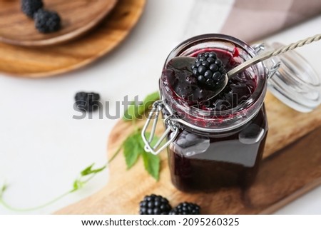 Jar of tasty blackberry jam on light background, closeup