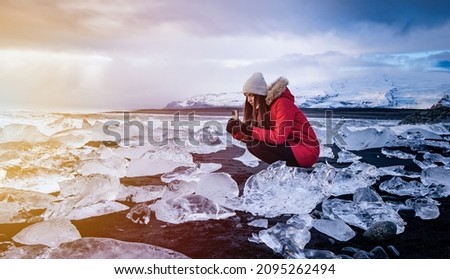 Girl taking a picture during sunset of a blue iceberg in ice lagoon at Iceland.  Woman taking photograph of beautiful Icelandic nature with Vatnajokull.