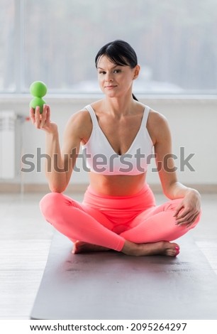 A brunette girl in a white top and coral leggings holds a massage ball in her hands.  Ball massager for yoga pilates or stretching and fascia pain. Sports and massage