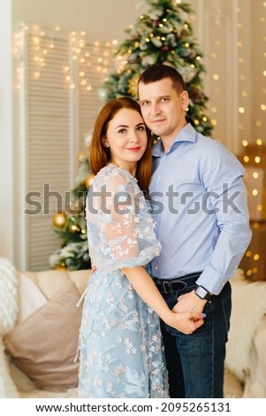 an attractive couple in love in blue clothes in the room by the Christmas tree. the tradition of celebrating the New Year at home and giving gifts. honeymoon in winter.