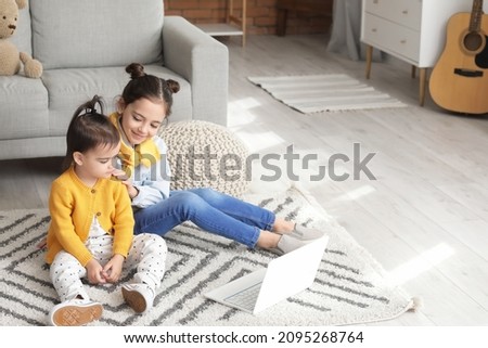 Cute little sisters with laptop watching cartoons at home