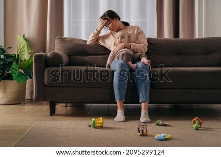 Postnatal depression and stressful motherhood concept. Exhausted woman feeling headache, holding her little baby, suffering from sleepless nights and problems. Single mom take care of her baby alone Royalty-Free Stock Photo #2095299124