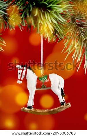 Christmas ornaments. rocking horse toy pendant on Christmas tree branch. Happy new year greeting card. Copy space banner. Red background with bokeh lights.