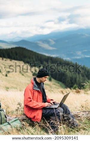 tourist freelancer in the mountains working online, laptop in travel for work, internet technologies for tourism, man sitting on the background of mountains, horizontal banner, freelance concept