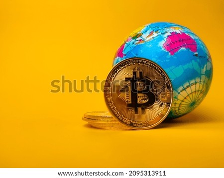 Bitcoins and world globe on a yellow background with copy space.