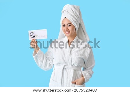 Young Asian woman with gift voucher for massage on color background