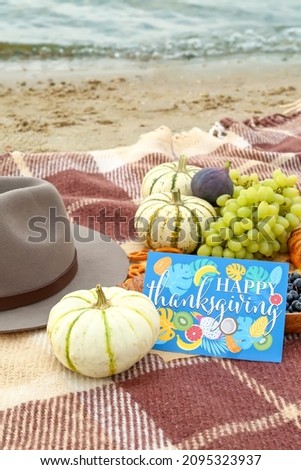 Delicious food, felt hat and card with text HAPPY THANKSGIVING on sand beach, closeup