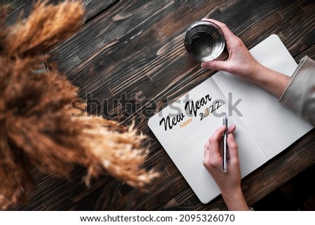 woman writes New Year's greetings and plans for the next year in a notebook top view. female hands
 with pen and notebook mockup