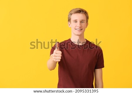 Handsome man with dental braces showing thumb-up gesture on color background