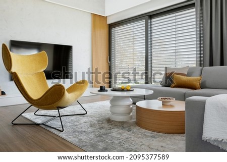 Modern living room interior design with corner beige sofa, creative rounded coffee tables, mustard armchair and personal accessories. Panoramic windows. Template. 