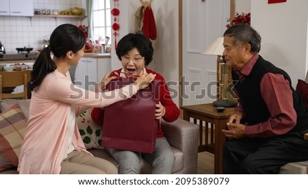 caring asian adult daughter going back to her mother's house during spring festival Chinese new year and giving gift bag to her elderly parents in the living room at home