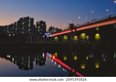 De-focused, blurred the view of the lights of bridges and buildings that light up at dusk reflecting on the water in the river.