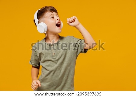 Little small happy boy 6-7 years old wearing green t-shirt headphones listen to music sing song in microphone isolated on plain yellow background studio. Mother's Day love family lifestyle concept. Royalty-Free Stock Photo #2095397695