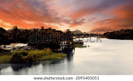 Dark contrast sunset in tropics on big river with village, bridge and mountains on background. The Bridge on the River Kwai, Thailand 5th of july 2009. High quality photo