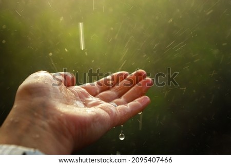 A hand of a woman, catching rain drops with blurred green background in summertime