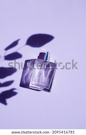 Transparent bottle of perfume on a purple background. Fragrance presentation with daylight. Trending concept in natural materials with plant shadow. Women's and men's essence. Royalty-Free Stock Photo #2095416781