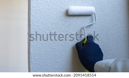 A worker who paints the outer wall with a paint roller. Royalty-Free Stock Photo #2095418554
