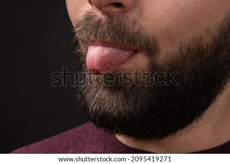close-up of cropped portrait of young bearded man showing tongue out, isolated on black background, emotion of fun, jokes. 