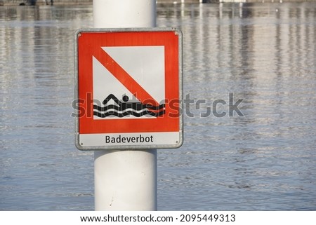 Square shaped signpost saying in German bathing prohibited attached on a metal pole. Placed in Lake Lucerne in Switzerland. The lake itself is on the background. It is warning symbol against danger.