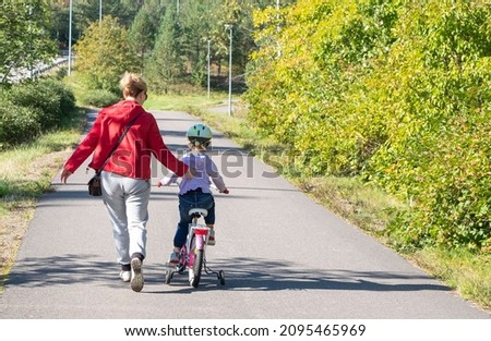 A girl, blonde, teaches a child to ride a bike. Walk on the bike path on a summer day