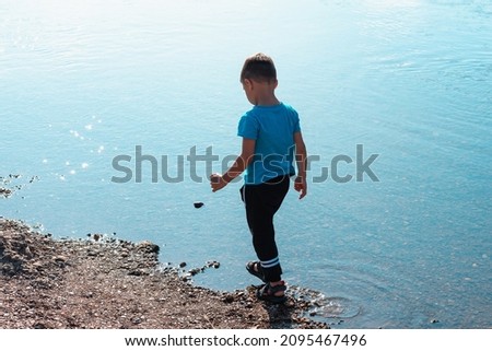 A boy on the river bank walks on small stones.