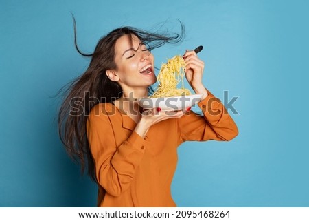 Delicious taste. Beautiful young girl eating delicious Italian pasta isolated on blue studio background. Holidays, traditions, food, popularity, cafe, love. Healthy carbohydrates. Copy space for ad Royalty-Free Stock Photo #2095468264