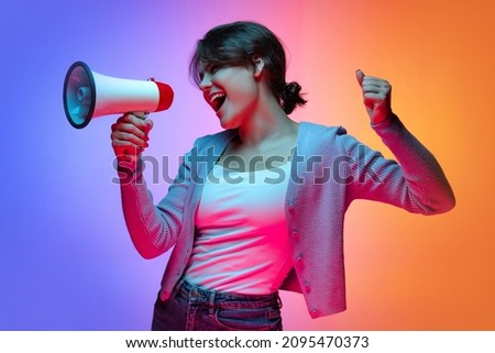 Attention, news. Excited young beautiful girl in warm cardigan shouting at megaphone isolated on gradient blue orange neon background. Concept of emotions, facial expression, youth, aspiration, sales Royalty-Free Stock Photo #2095470373