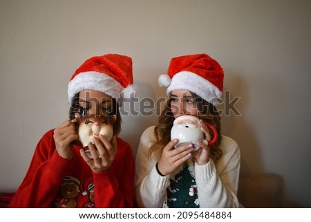 Two Caucasian females wearing Santa Claus hats and drinking hot chocolate on Christmas