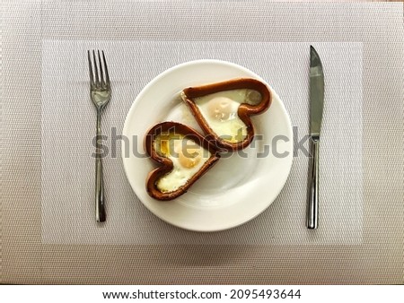 14 Valentine's Day Breakfast. Fried egg inside heart shaped sausage in a white plate. Fried chicken eggs for breakfast. A delicious dish of eggs with yolk and protein. High quality photo Royalty-Free Stock Photo #2095493644